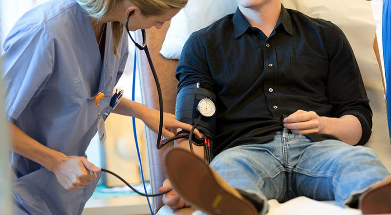 Sköterska tar blodtryck på ung man som sitter på brits
