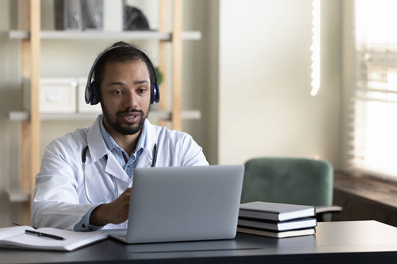 Läkare med hörlurar sitter vid dator och har ett digitalt möte med patient