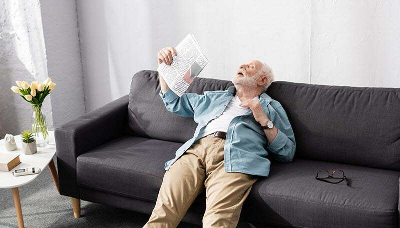 Äldre man fläktar sig med tidning i varmt rum.