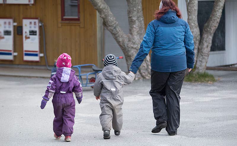 Förskolelärare och förskolebarn i vinterkläder utomhus på förskolegård