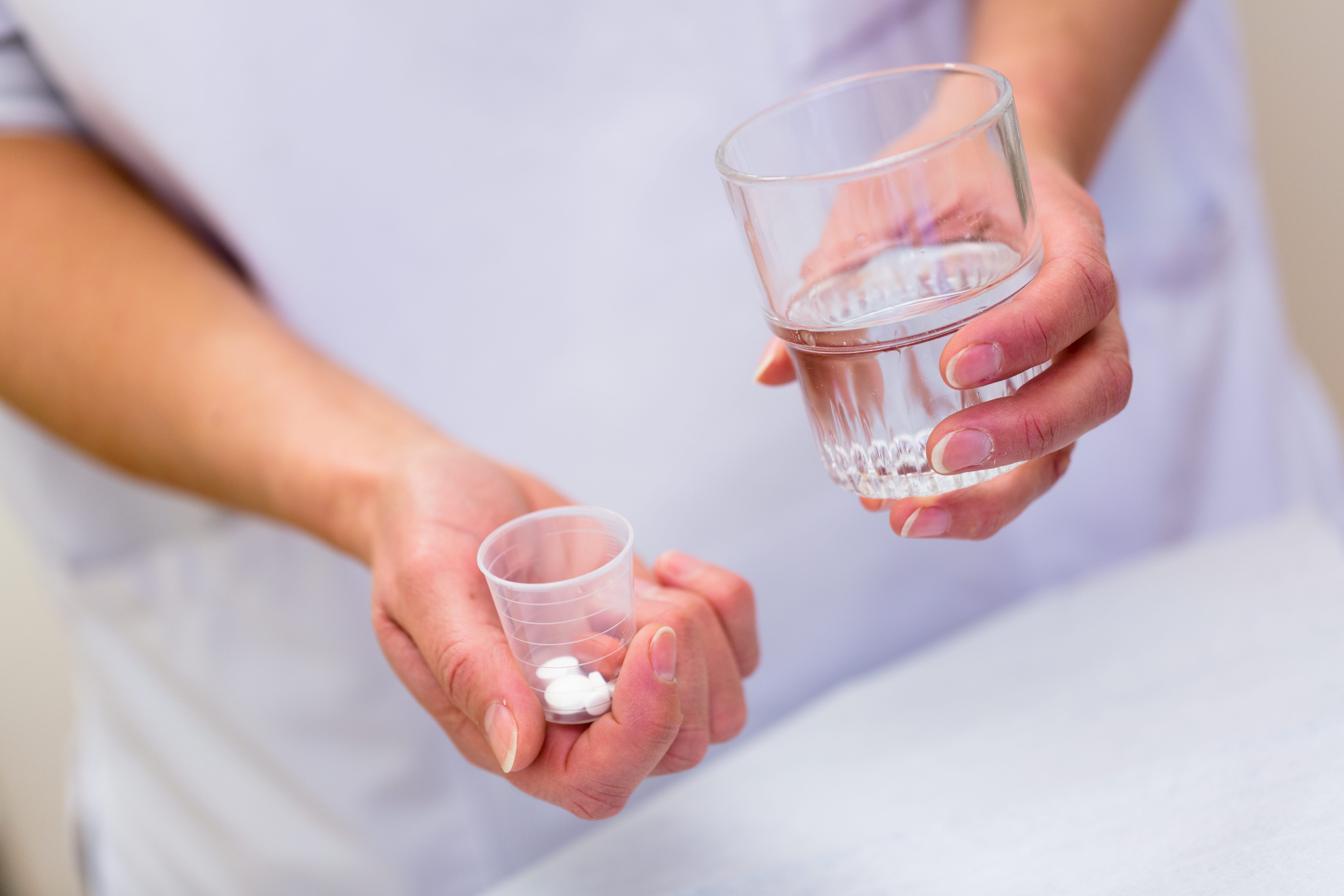En person håller ett glas med vatten och en liten plastkopp med vita piller. Foto: Yanan Li