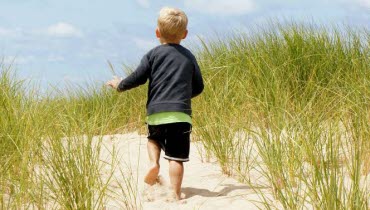 Litet barn går i sanddyna med ryggen mot kameran