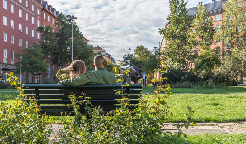 Par på parkbänk i parkområde mellan husen i Stockholm.