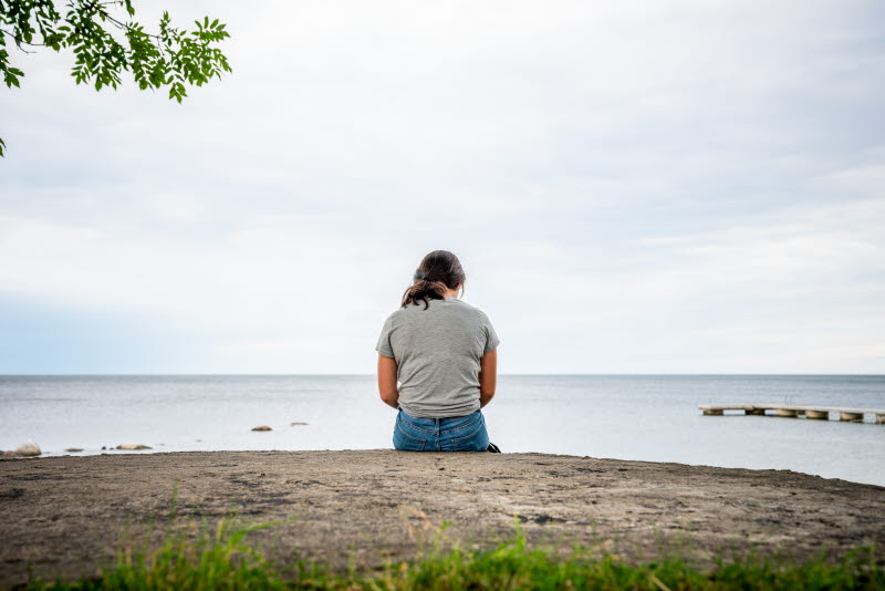 En kvinna sitter ensam vid en strandkant. 