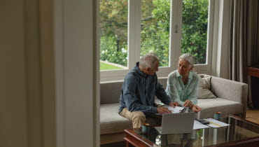 Äldre par som sitter i en soffa och diskuterar i sitt vardagsrum.