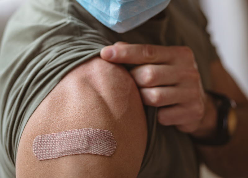 En person i munskydd visar upp sin arm med ett plåster på efter vaccintion. 
