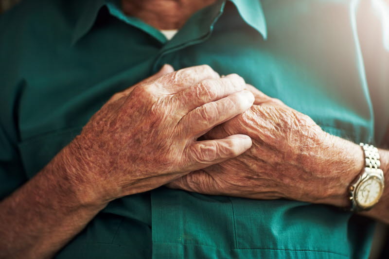 en äldre man håller sina händer över bröstet