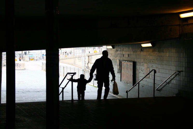 Siluett av en man som håller ett barn i handen på väg uppför en trappa i stadsmiljö
