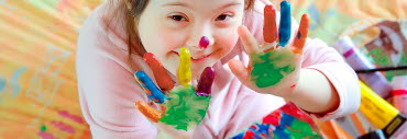 Ett barn leker med färg och håller upp sina målade handflator