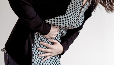 En person håller händerna för magen och böjer sig framåt. 