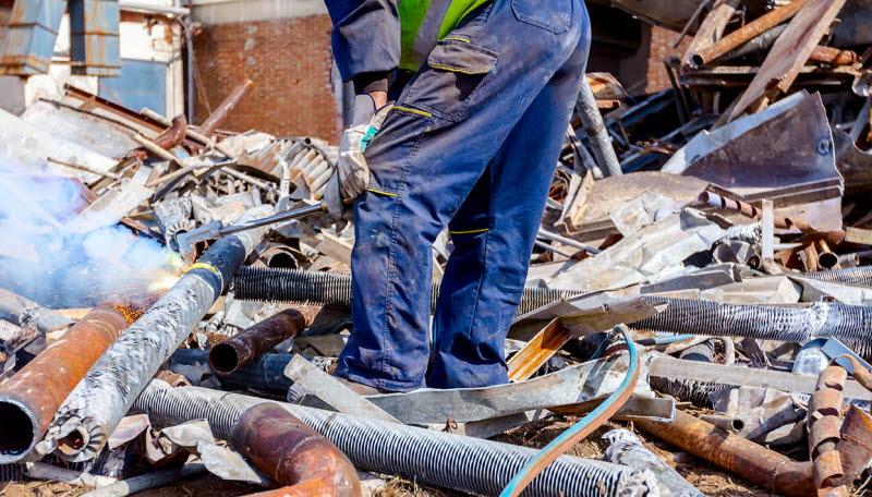Manlig arbetare skär metall med skärbrännare på återvinningscentral