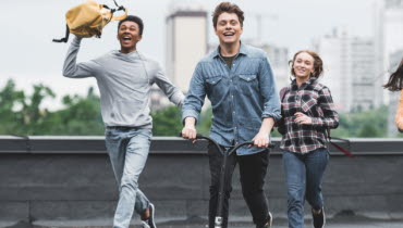 Tre tonåringar springer mot kameran, en åker sparkcykel och alla ler.