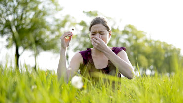 Ung kvinna i högt gräs som nyser med handen för näsan och med en näsduk i andra handen.