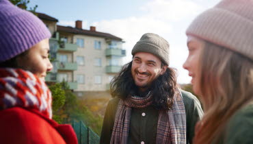 tre unga personer står utomhus och har ett samtal och ler