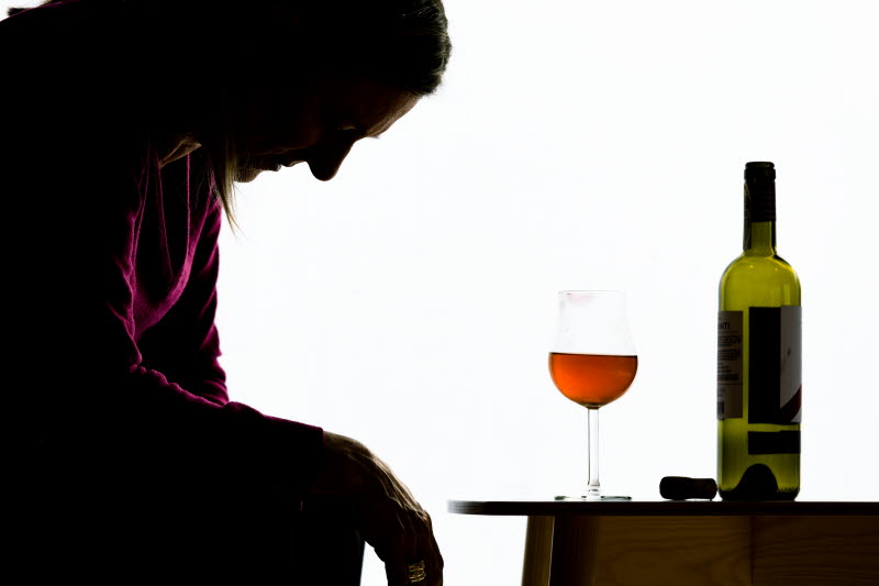 Kvinna sitter framåtlutad framför bord med vinglas och vinflaska