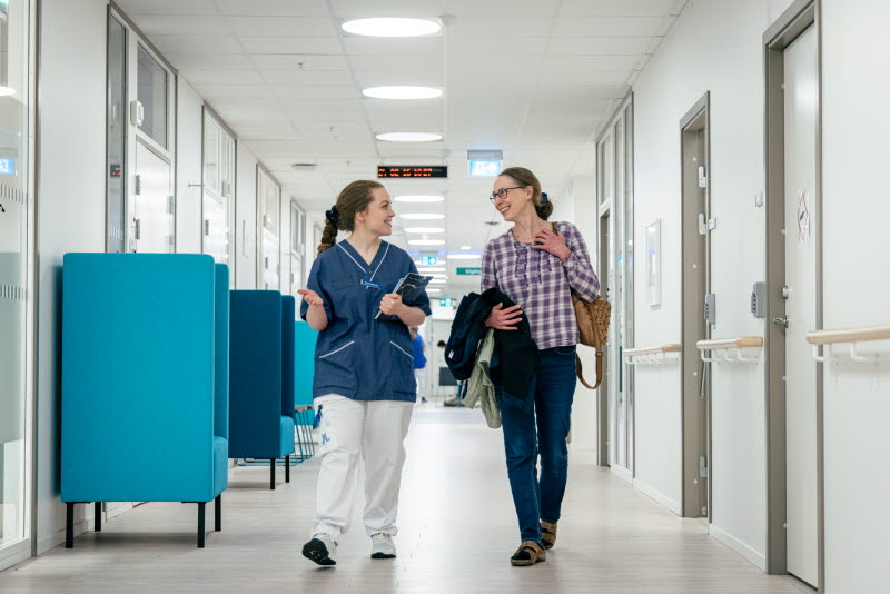 En sjuksköterska och en patient går i en korridor, båda ler. Foto: Yanan Li