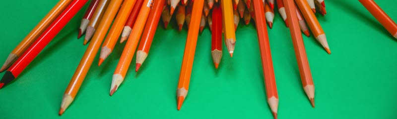 En bunt med orange färgpennor mot grön bakgrund
