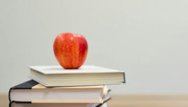 Rött äpple på böcker, pennor och a-, b- c-klossar.