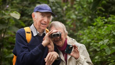 en äldre man och en äldre kvinna tittar i en kikare och ler mot kameran