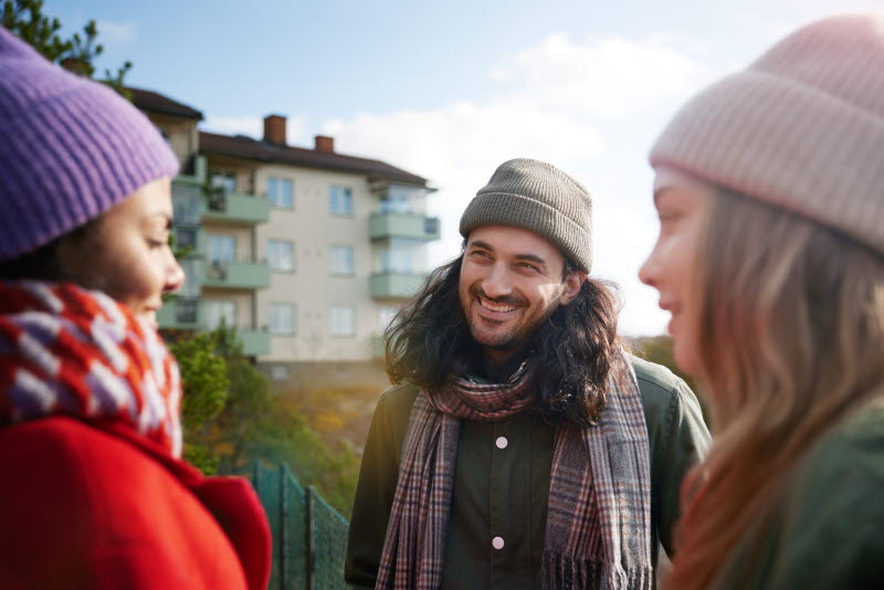 tre unga personer står utomhus och har ett samtal och ler